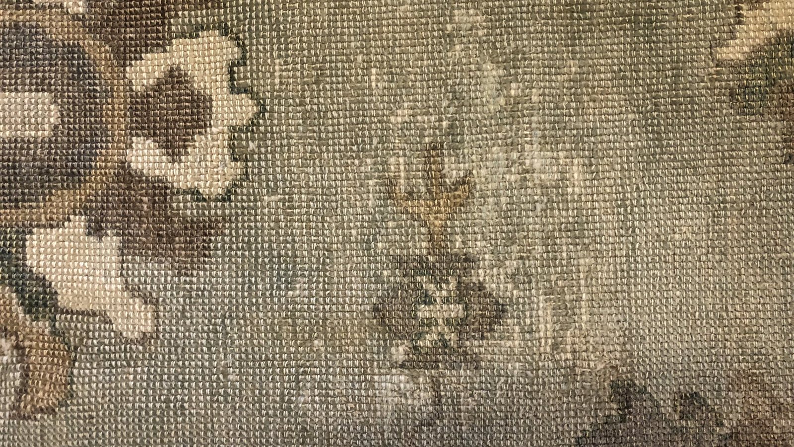 The reverse of a wool rug under inspection light, with fine sand visible down in the foundation